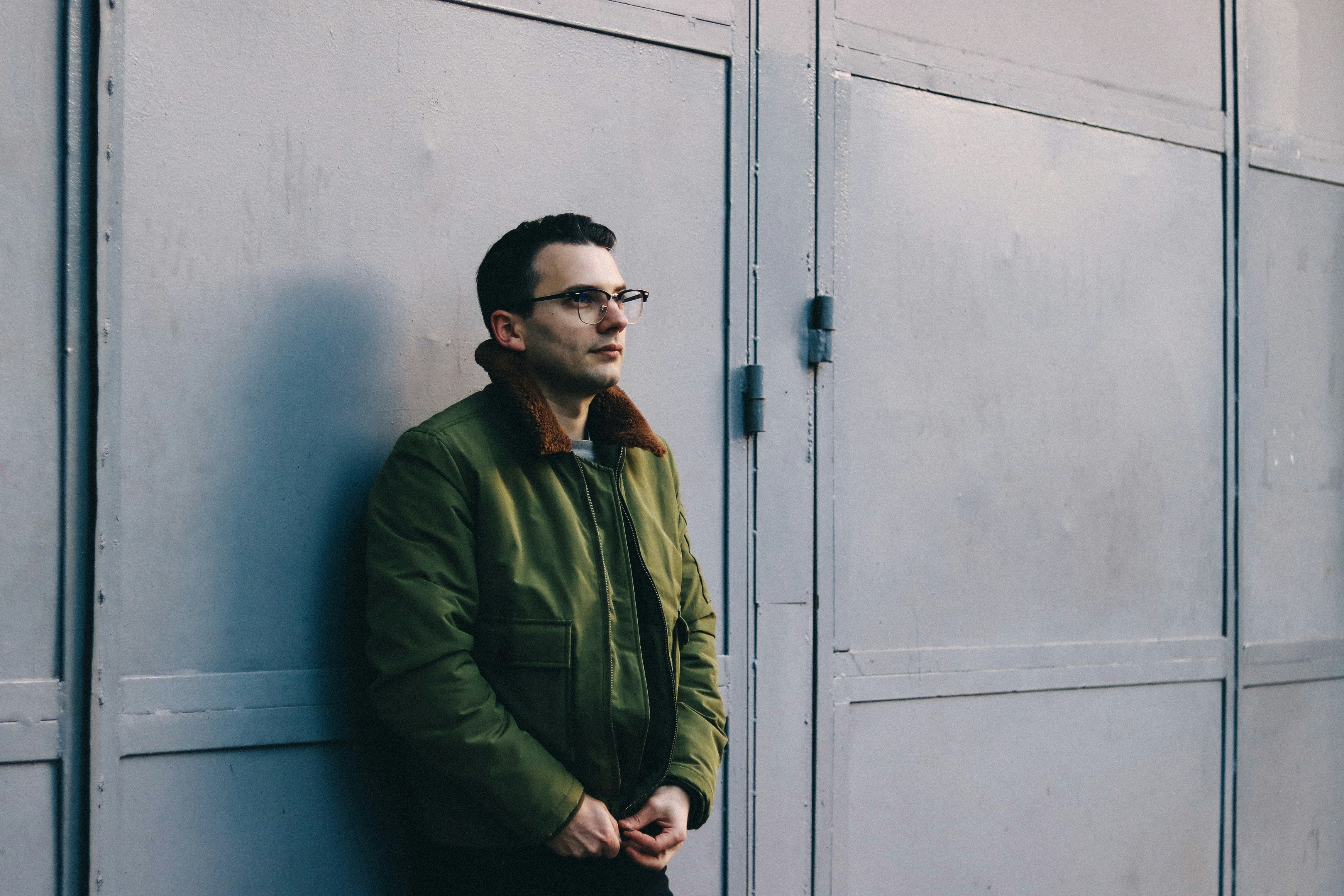 man in green jacket standing beside blue wooden door